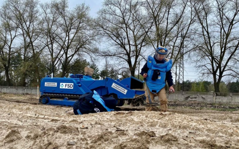 Ukrainian women demining a field in front of a mine resistant vehicle