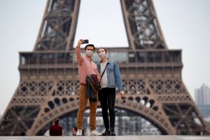 Masked tourists take a photo in front of the Eiffel Tower