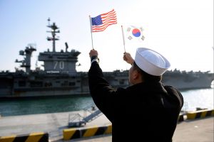 A ROK sailor waves flags in front of an aircraft carrier