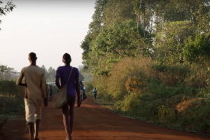 Two people walking down a dirt road with trees in the background