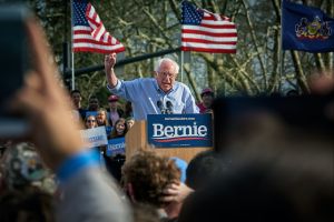 Bernie Sanders speaking at a podium to a crowd of supporters