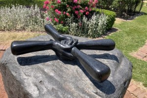 Helping hands sculpture in Chicago in front of a rose bush and lawn.