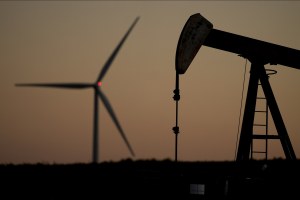 A pumpjack operates in the foreground while a wind turbine at the Buckeye Wind Energy wind farm rises in the distance