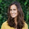 Dr. Priya Fielding-Singh is pictured from the shoulders up wearing a yellow sweater standing in front of a green background. She looks into the camera smiling.