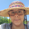 Ife Kilimanjaro is pictured from the shoulders up, wearing a light gray shirt, striped hat, and glasses as she smiles into the camera.