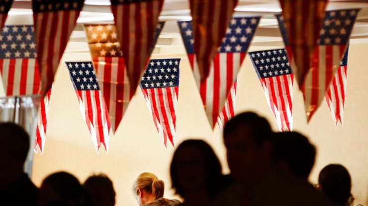 a crowd stands under American flags