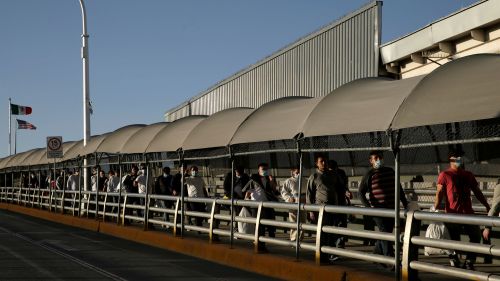 Mexican immigrants walk across a bridge at the US border after being deported during the COVID-19 pandemic