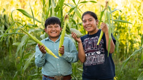 Doyan and Kaiesta smile into the camera as they hold up two stalks of corn.