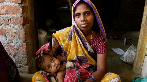 Shyamkali sits cross legged and holds her young daughter.