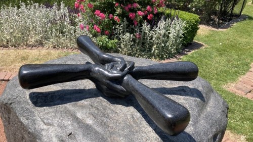 Helping hands sculpture in Chicago in front of a rose bush and lawn.