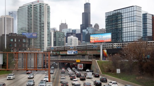 Traffic on I-90 with a Metra commuter train crossing overhead