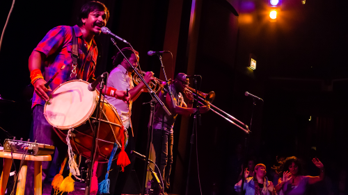 People with instruments perform on stage behind standing microphones