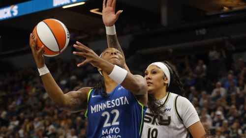 A woman in a blue Minnesota Lynx jersey shoots a basket while a woman in a white Chicago Sky jersey tries to block her