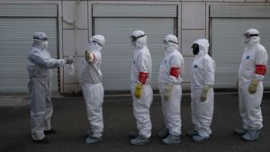 Volunteers in protective suits line up to be disinfected