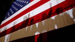 Shadows cast from a crowd of people in front of an American flag.