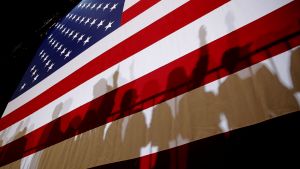  Shadows cast from a crowd of people in front of an American flag.