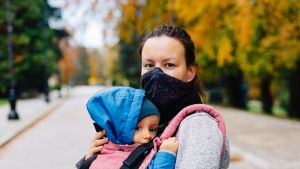 A woman wearing a mask with her child strapped to her chest. 