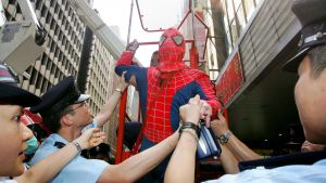 Police officers escort man dressed as Spiderman away after he installed banner in front of big screen in central Hong Kong.