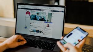 A person scrolls through social media on a laptop and a mobile phone.