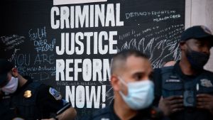 Police officers stand in front of sign that reads "Criminal Justice Reform Now!"