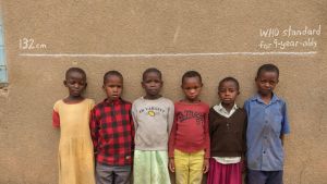 Six children standing under a line in chalk against a wall, which reads "WHO Standard for 9 year olds"