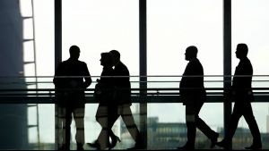 Silhouettes of five people are seen walking through a hallway with glass windows