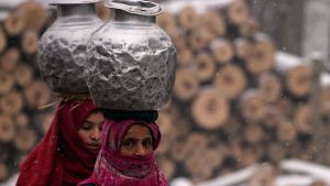 Two women carry water through snow in Pattan, India