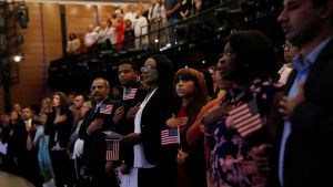 New citizens stand, while holding small American flags, during the National Anthem at a U.S. Citizenship and Immigration Services actualization ceremony.