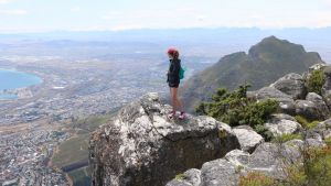 A person stands on a rock, with an aerial view of Cape Town behind them