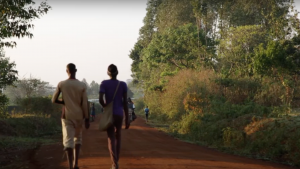 Two people walking down a dirt road with trees in the background