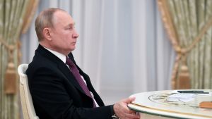 Vladimir Putin sits in profile at a table in front of white and gold curtains in meetings with Iran.