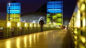 Figure walking on Berlin bridge lit up in Ukrainian flag colors. 