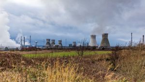 Smokestacks on the horizon of a field with stormy skies.