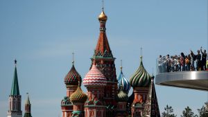 People walk in front of St. Basil's Cathedral on the pedestrian bridge over Moskva river at the Zaryadye Park off Red Square in central Moscow