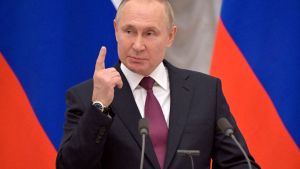 Vladimir Putin standing in front of Russian flags pointing.