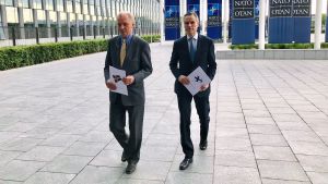 Two men walking in front of a building holding files