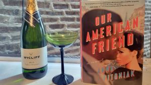 Bottle of wine, glass and book in front of a brick wall.