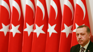 Turkish President Recep Tayyip Erdogan sits in front of a row of Turkish flags.