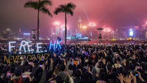 A large crowd of people celebrate New Year's Eve 2020 in Hong Kong, with 'free HK' neon letters in the foreground.