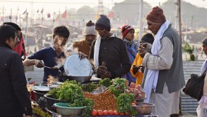 Two men purchase food from a food stall outside.