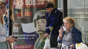 People wait a bus at a bus stop with an army recruiting billboard calling for a contract for service in the Russian armed forces