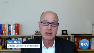 Paul Heer on Zoom speaking to VOA with bookshelf in the background and a white wall.