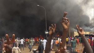 With the headquarters of the ruling party burning in the back, supporters of mutinous soldiers demonstrate in Niamey, Niger, Thursday, July 27 2023.