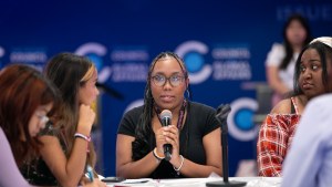 Black student holds mic in center of frame, seated and surrounded by other girls.