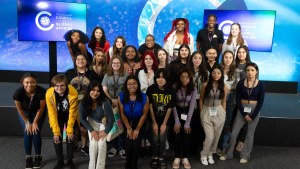 Large group of high school girls smile and pose together in front of Council backdrop. 