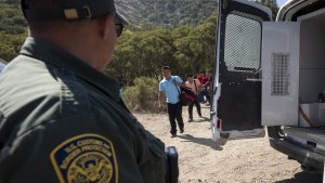 A Border Patrol agent leads a group of migrants seeking asylum towards a van