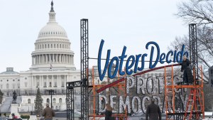  With the US Capitol in the background, people walk past a sign that says Voters Decide Protect Democracy