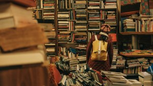 A person wearing a backpack browses shelves at a bookstore.